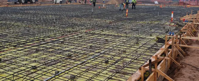 Wide-angle view of a 100,000 sq ft industrial foundation in Albuquerque featuring 12-inch compacted roadbase, vapor barrier, and a double mat of #5 rebar on 16-inch centers with structural anchor bolts for a metal building.